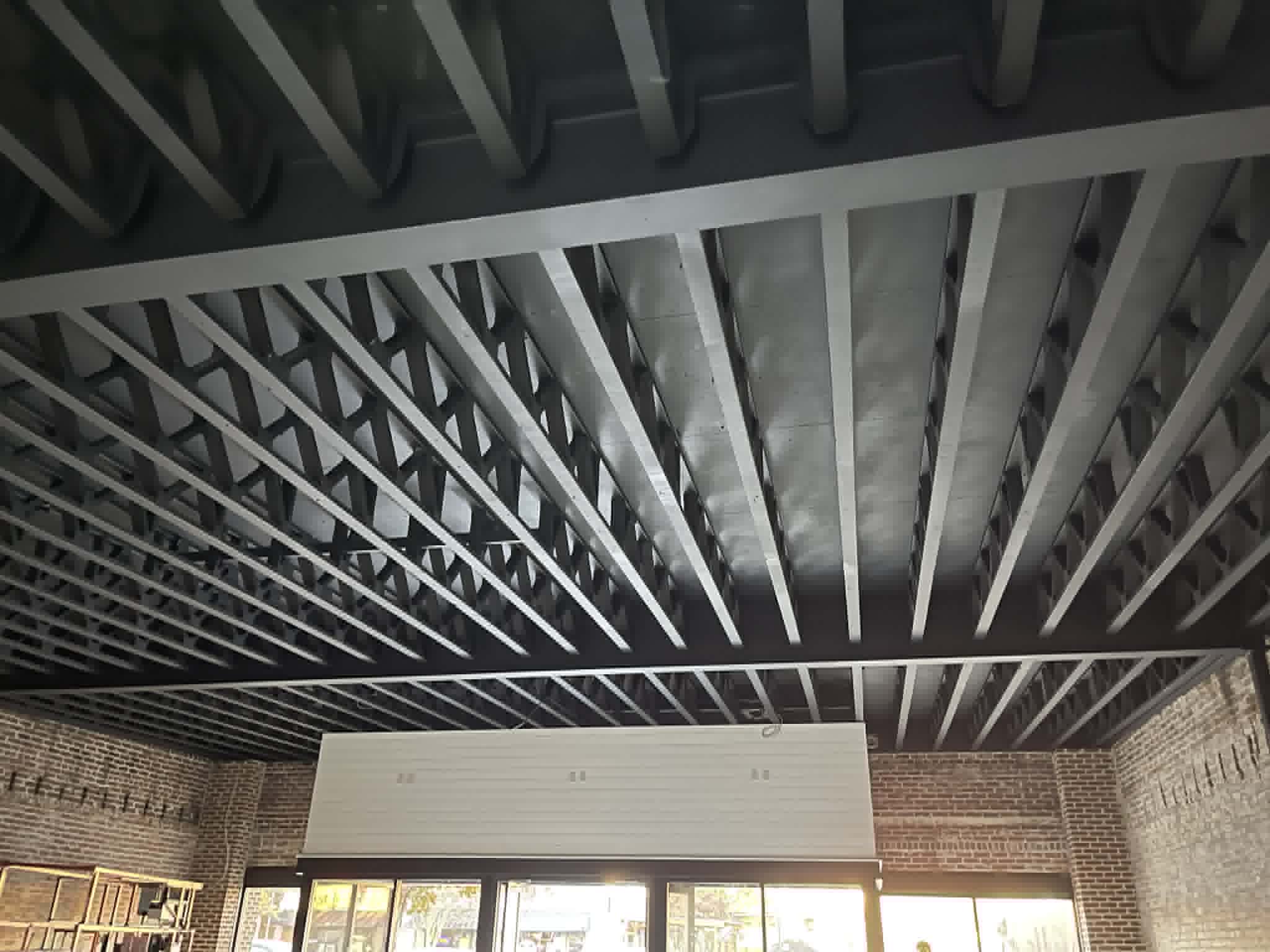 Commercial interior ceiling painting by Carlson Painting Co. featuring a uniform black dryfall finish on exposed structural steel joists and deck in a modern brick-walled retail space
