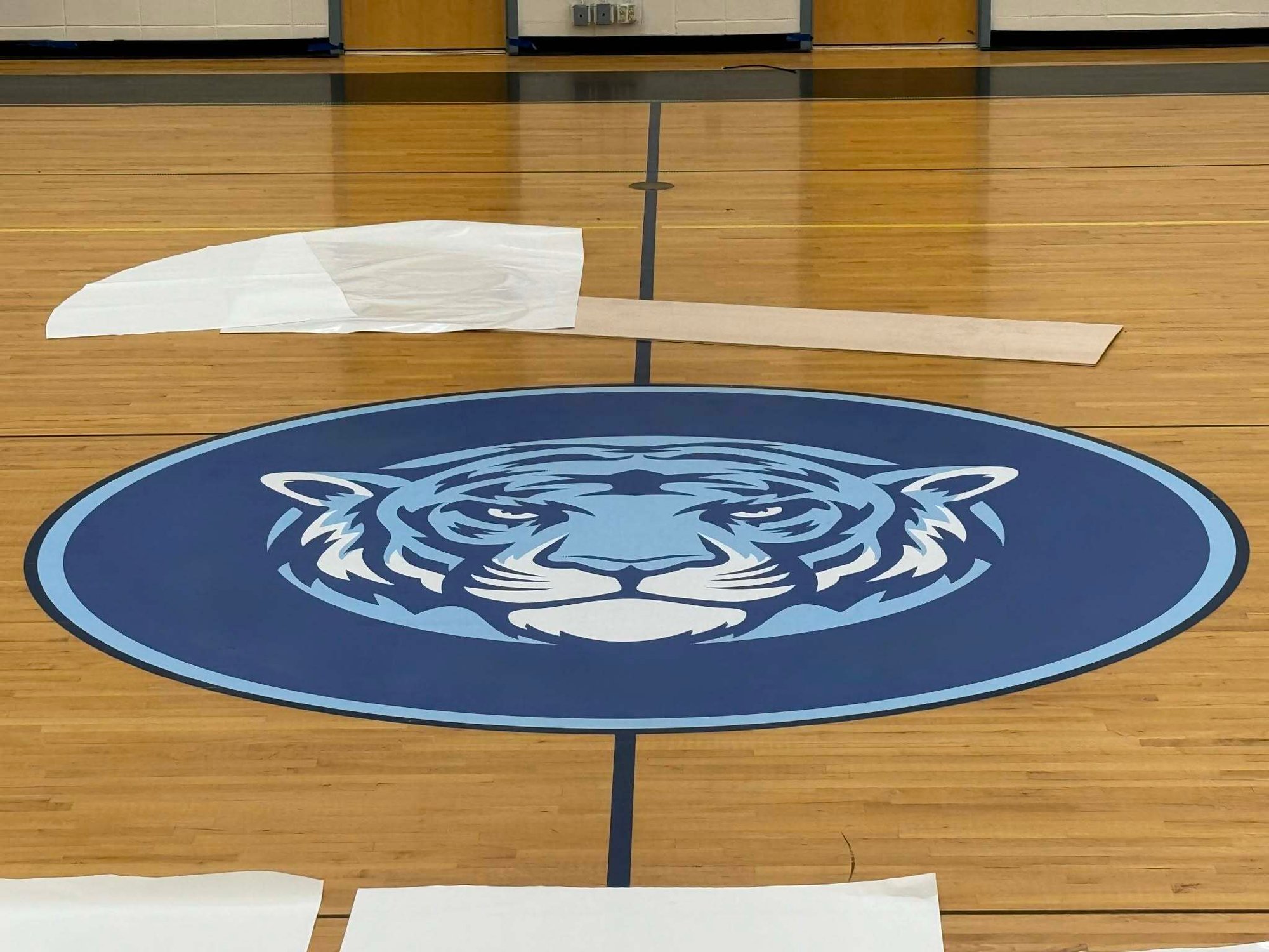 Carlson Painting Co. professional commercial interior finishing featuring a precision-painted school logo on a polished hardwood gymnasium floor. Carlson Painting Co. professional commercial interior finishing featuring a precision-painted school logo on a polished hardwood gymnasium floor.